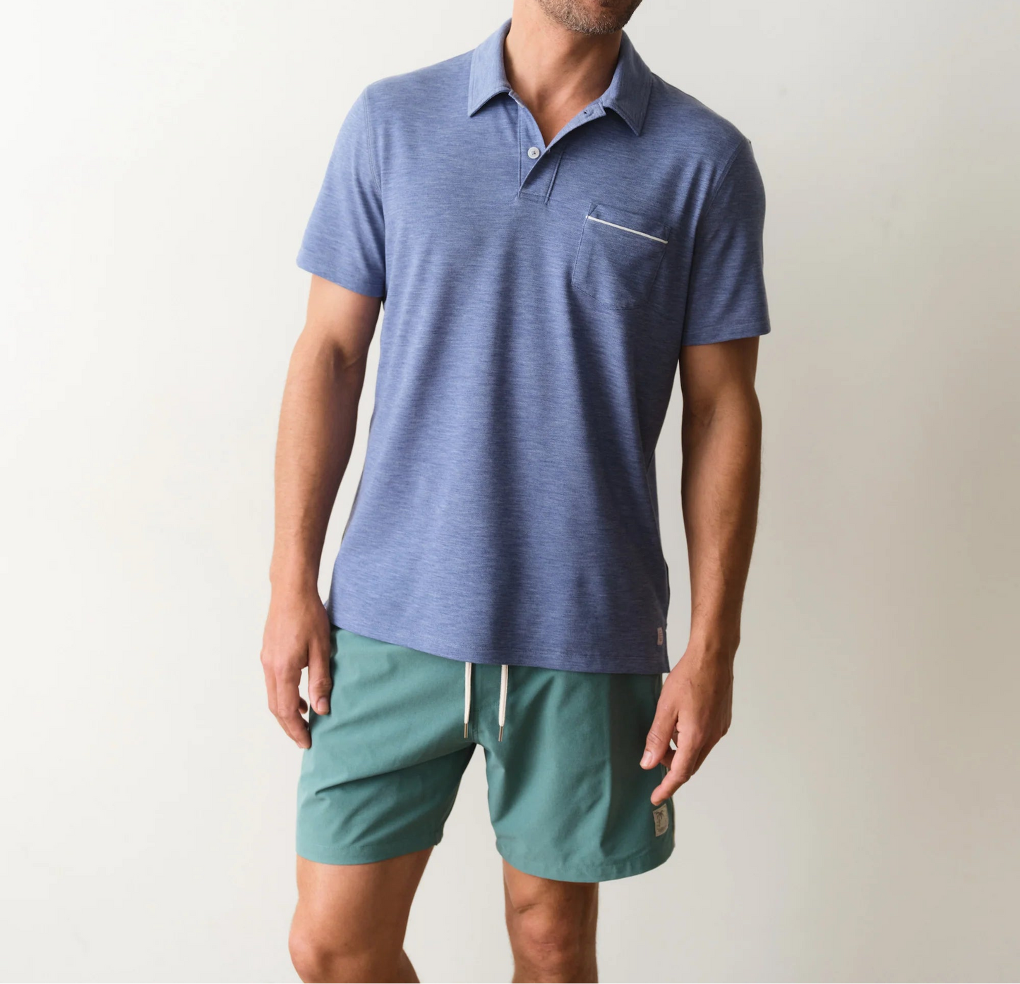Man wearing a blue polo shirt and green shorts on a plain background