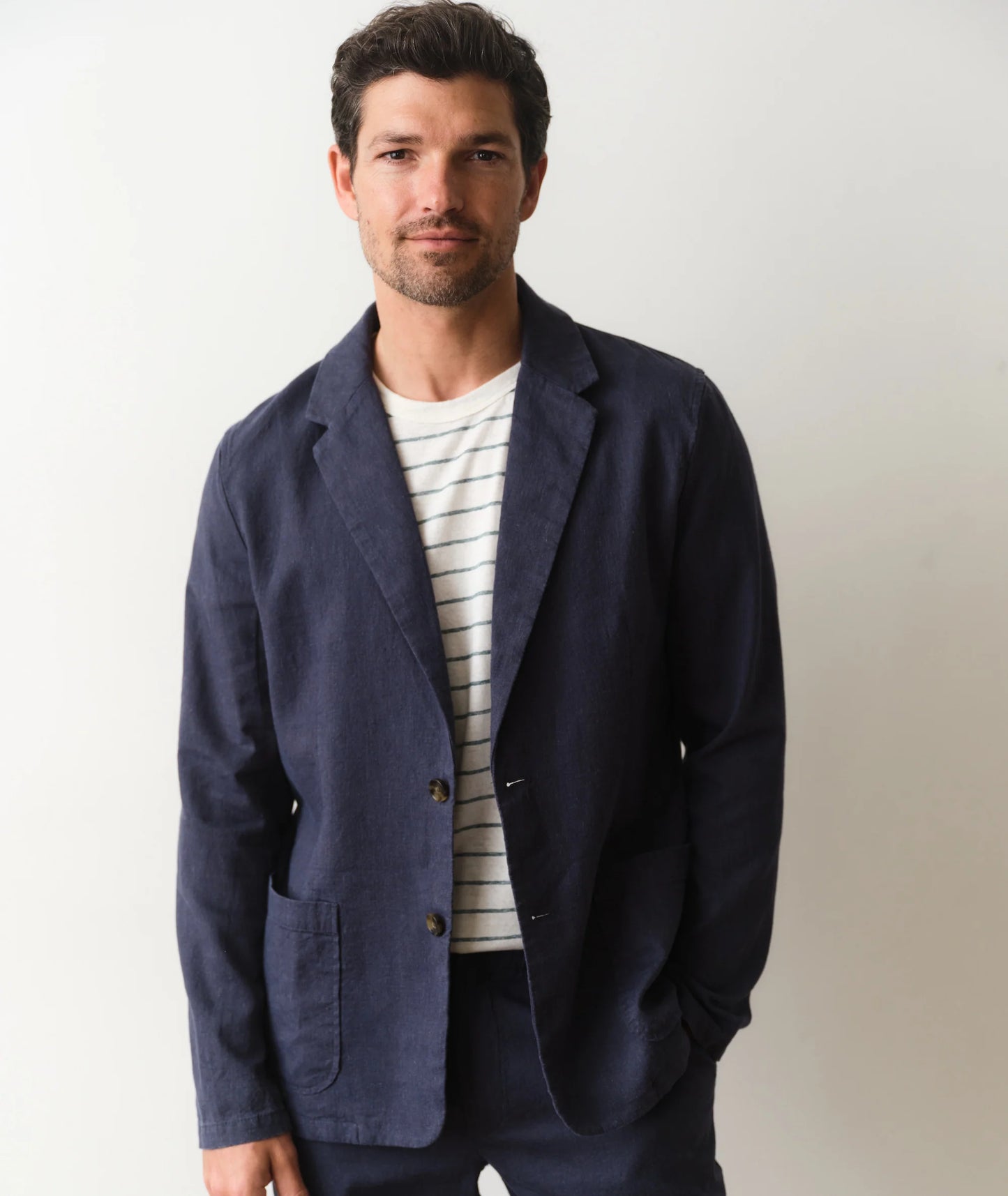 Man wearing a navy blazer over a striped shirt on a plain background