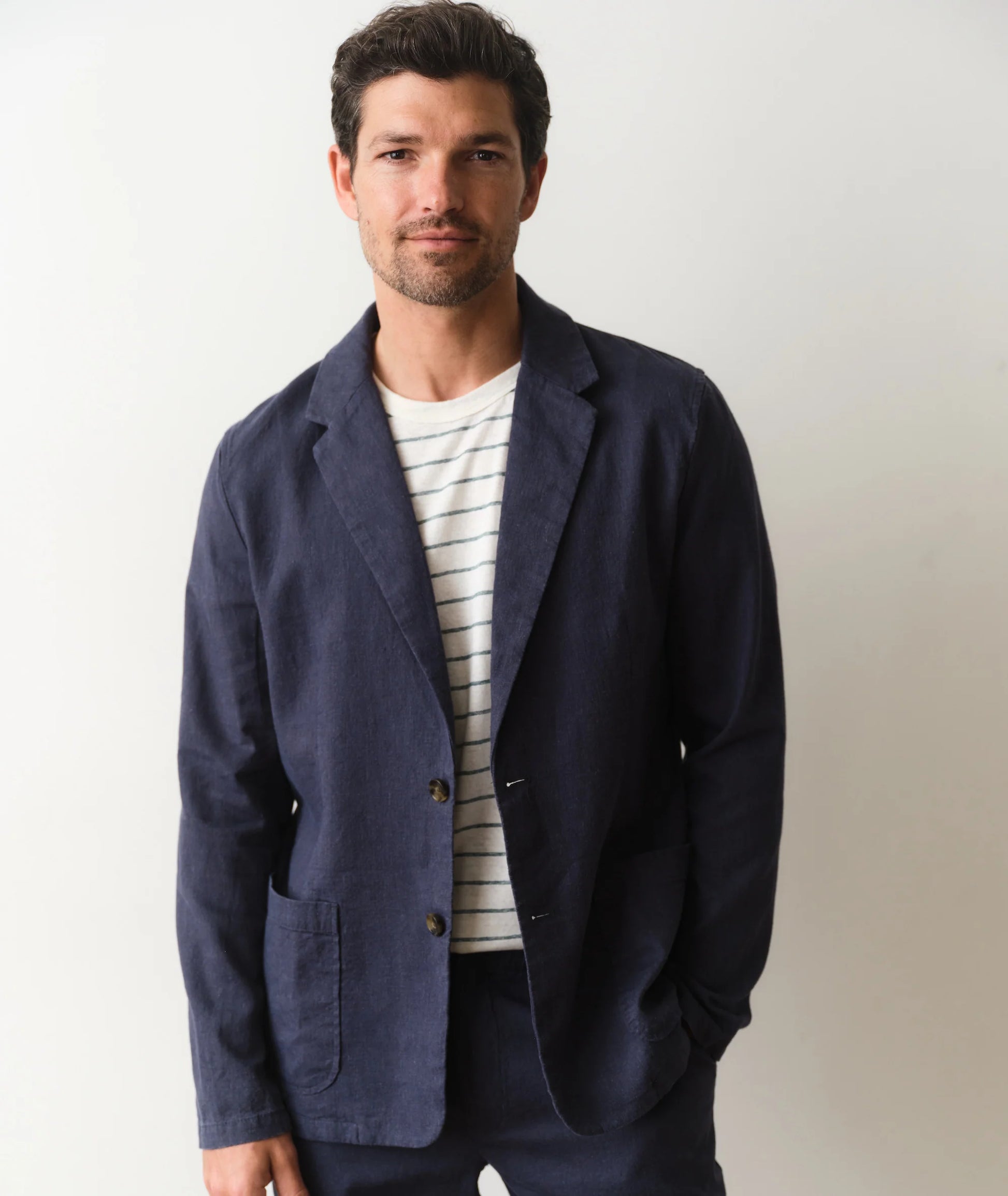 Man wearing a navy blazer over a striped shirt on a plain background