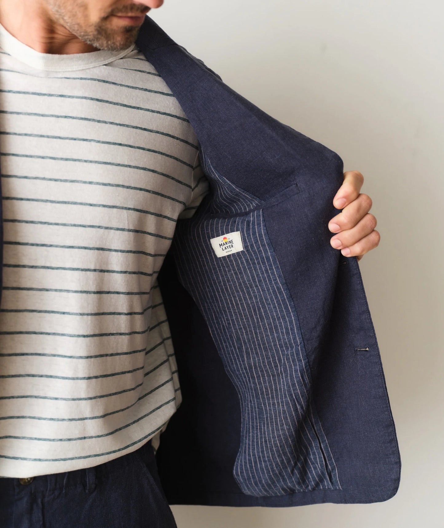 Person holding a navy pinstripe blazer with a visible brand logo on a plain background