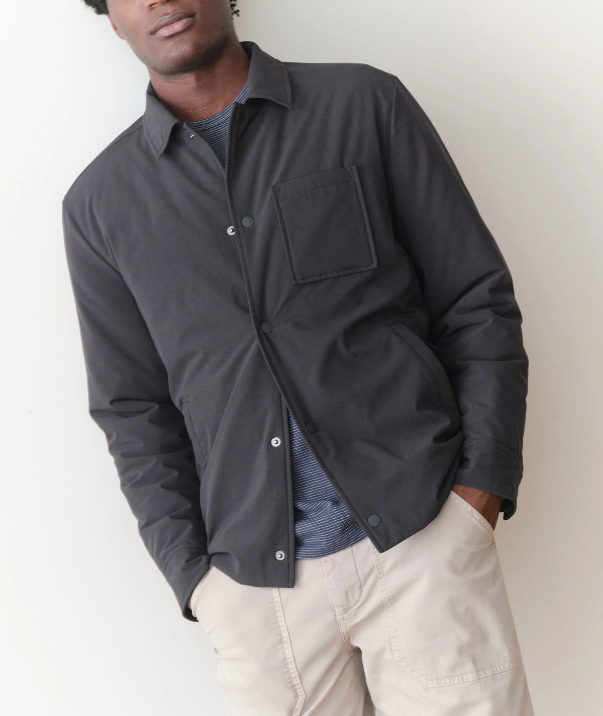 Man wearing a dark jacket over a shirt with beige pants against a white background