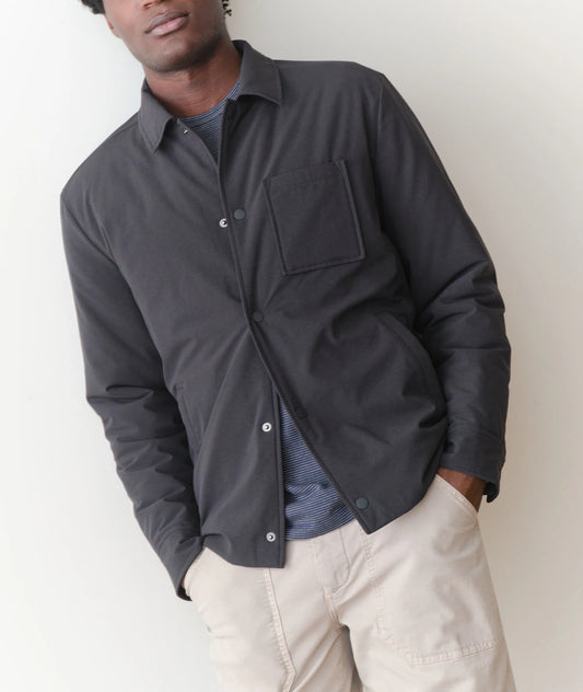 Man wearing a dark jacket over a shirt with beige pants against a white background