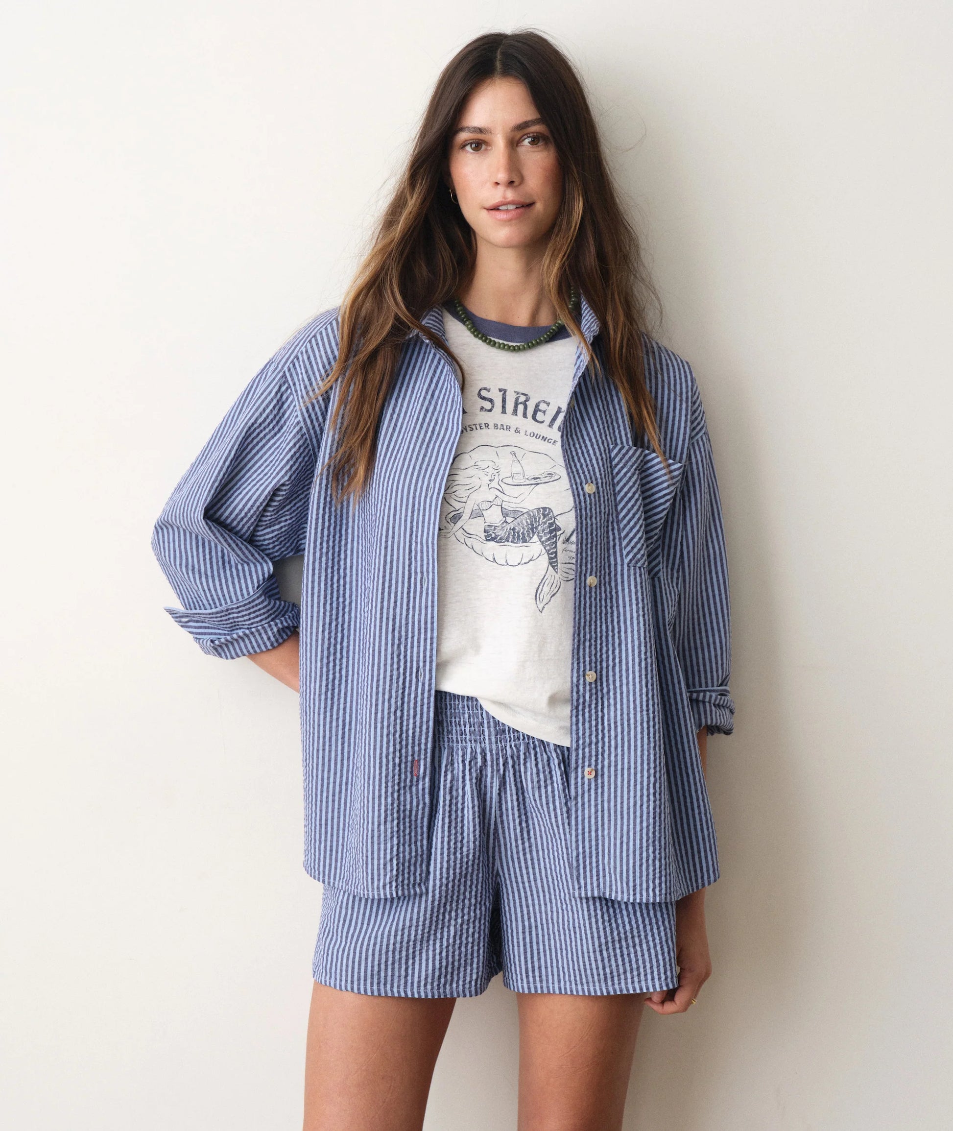 Woman wearing a blue striped shirt and shorts set over a graphic t-shirt on a plain background