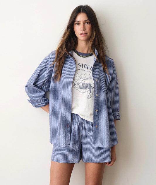 Woman wearing a blue striped shirt and shorts set over a graphic t-shirt on a plain background