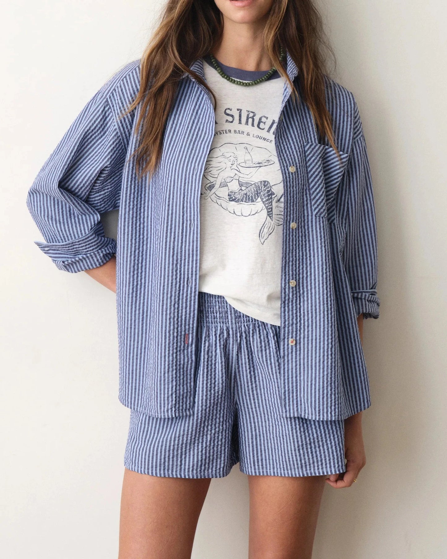 Woman wearing a blue striped shirt and shorts set with a white t-shirt underneath on a plain background