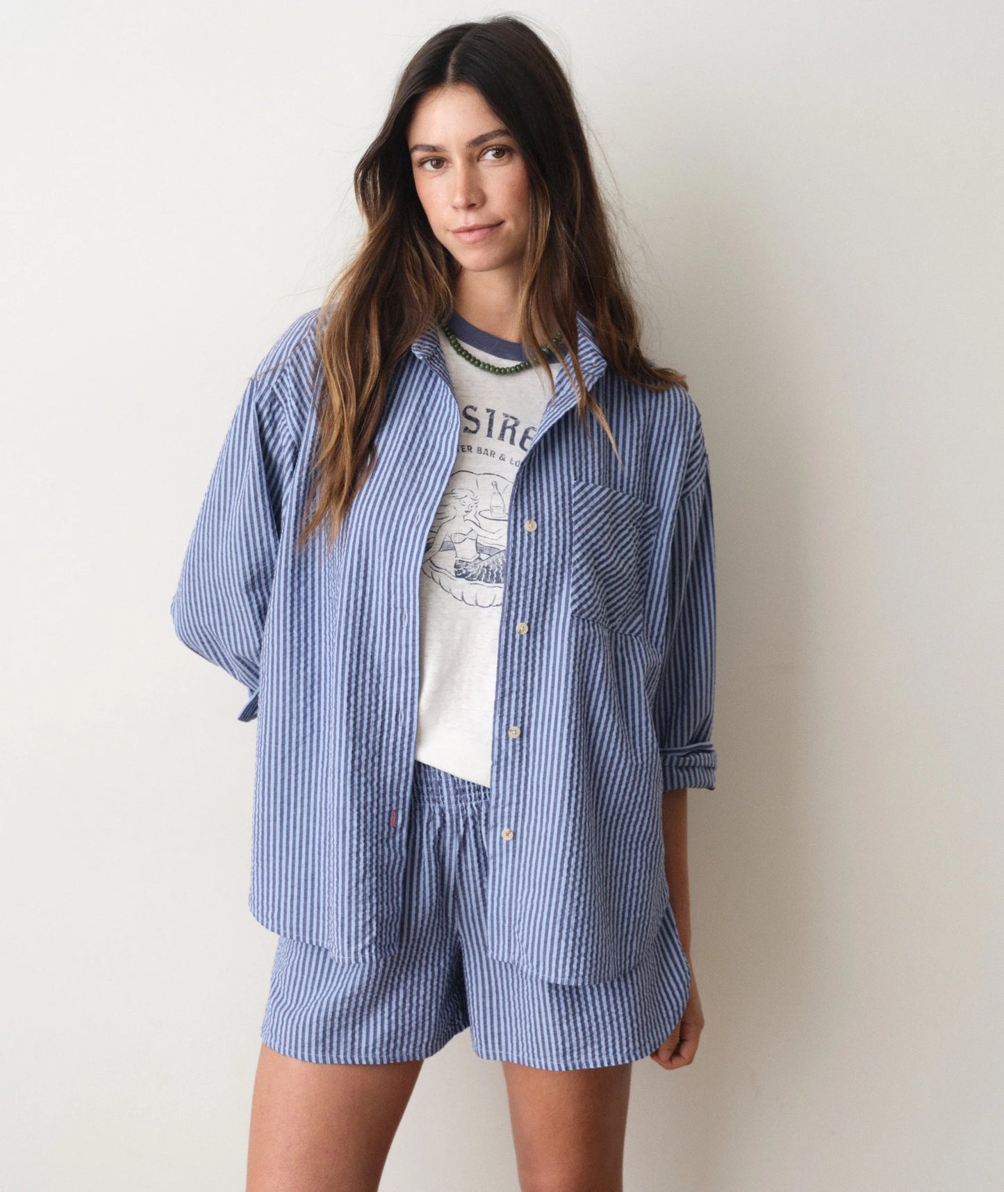 Woman wearing a blue striped shirt and shorts set over a graphic t-shirt on a plain background