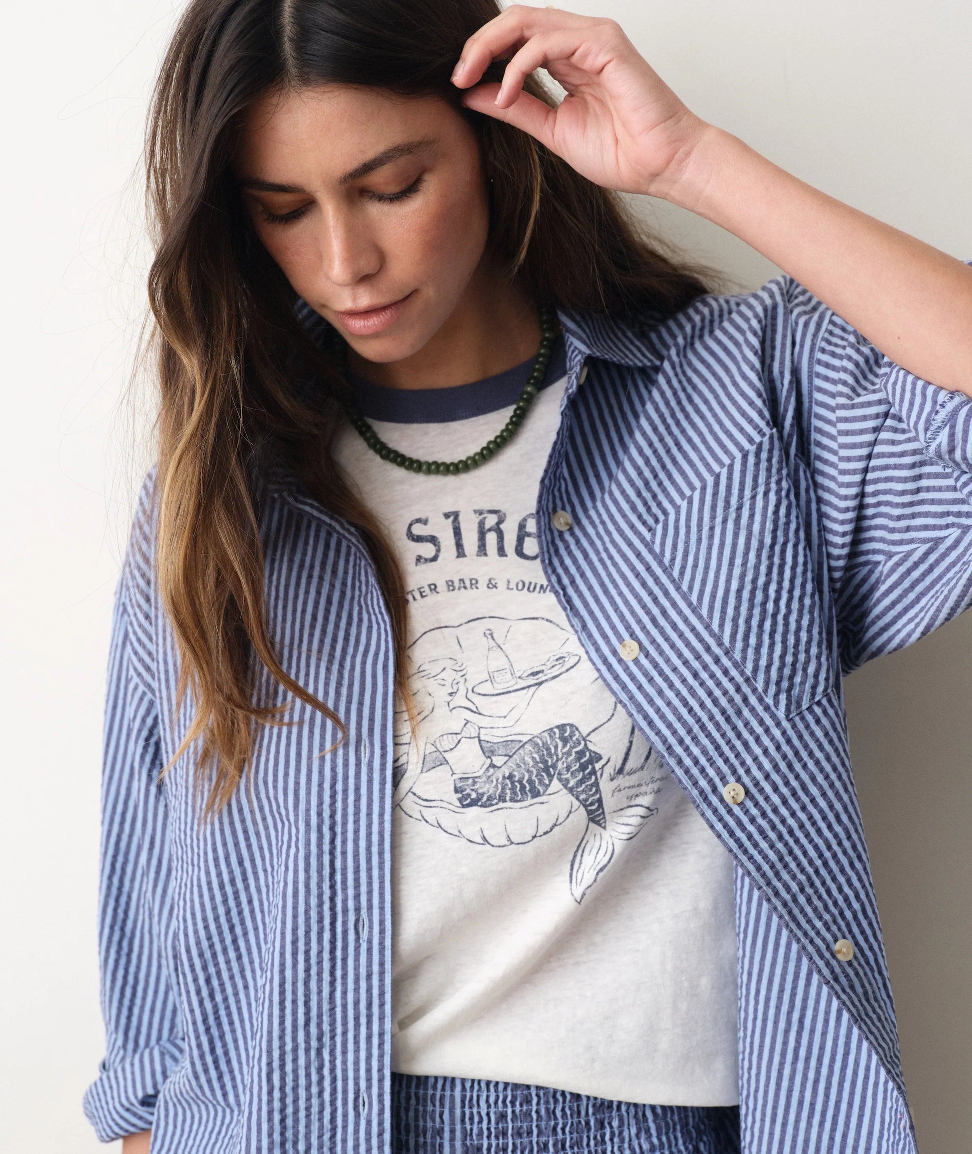 Woman wearing a white graphic t-shirt under a blue striped shirt with a neutral background