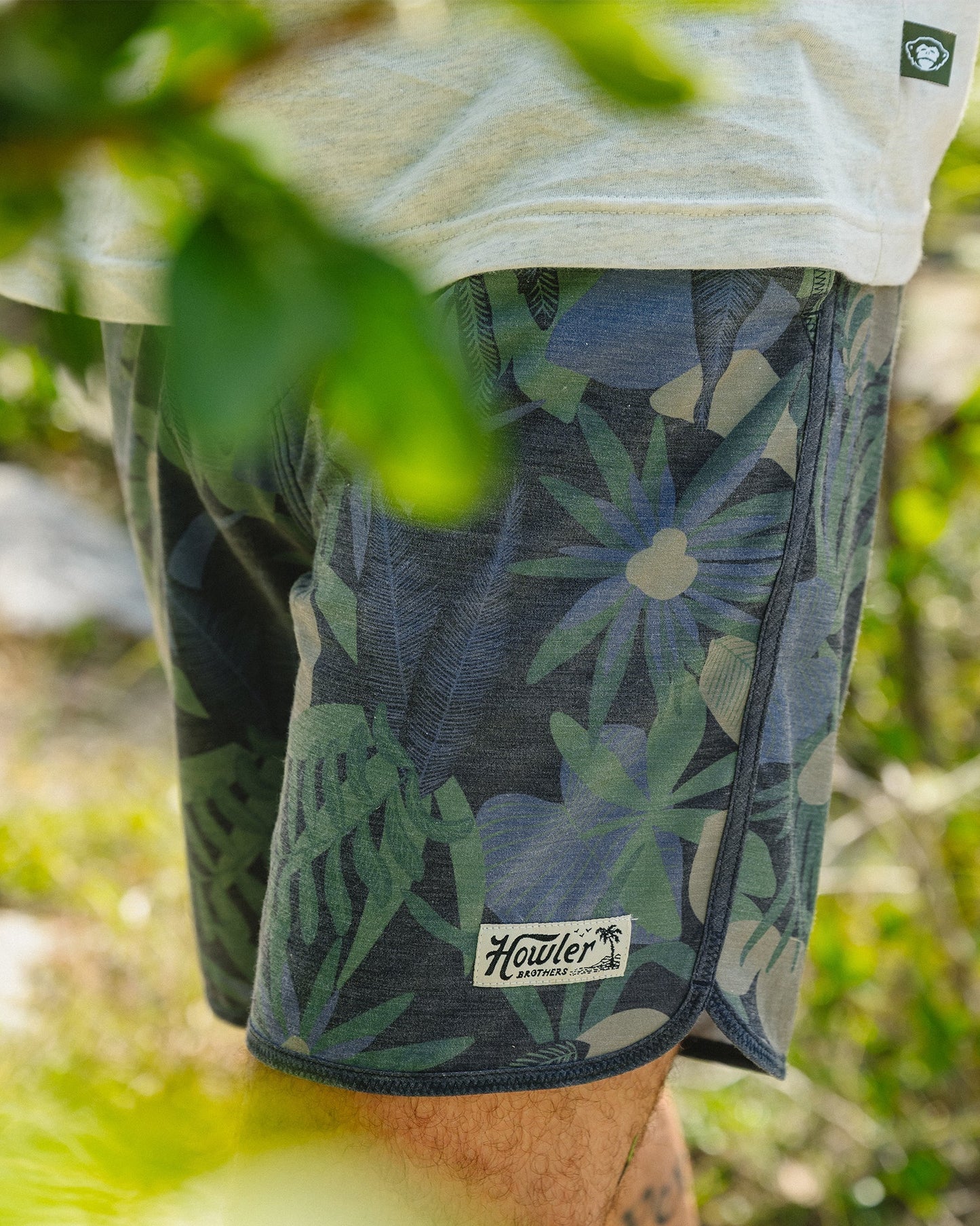 Person wearing floral shorts with a brand logo in a natural setting