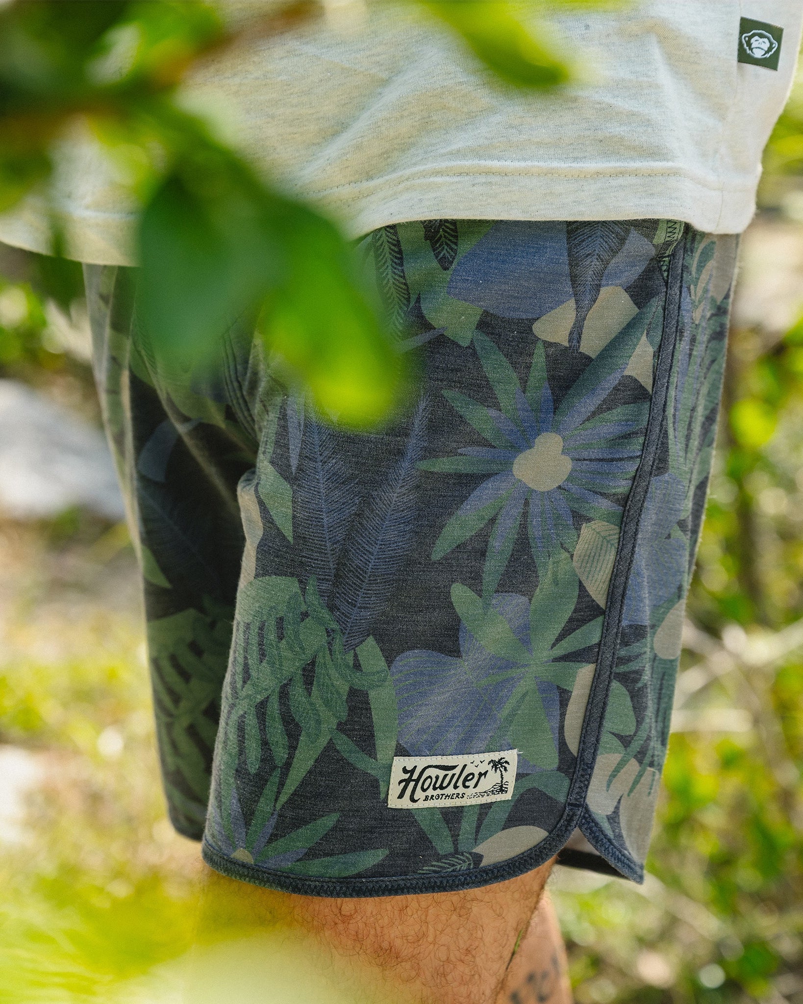 Person wearing floral shorts with a brand logo in a natural setting