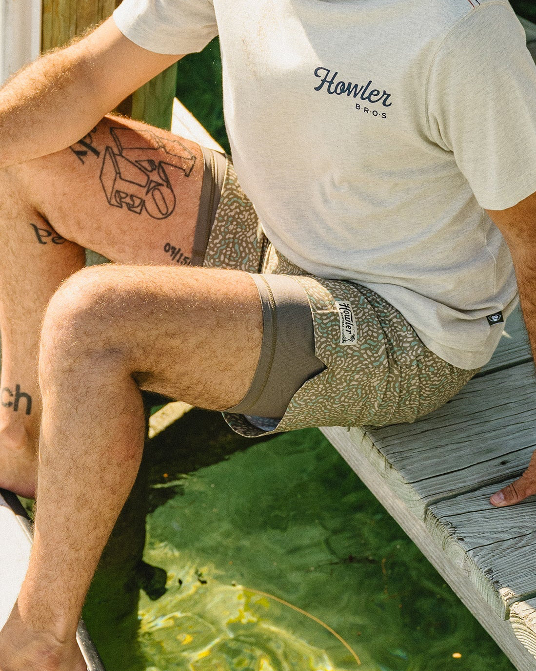 Man sitting on a dock by a body of water, wearing a Howler Bros t-shirt.