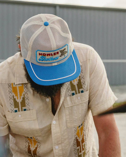 Man wearing a blue cap with a logo, looking down, against a blurred background