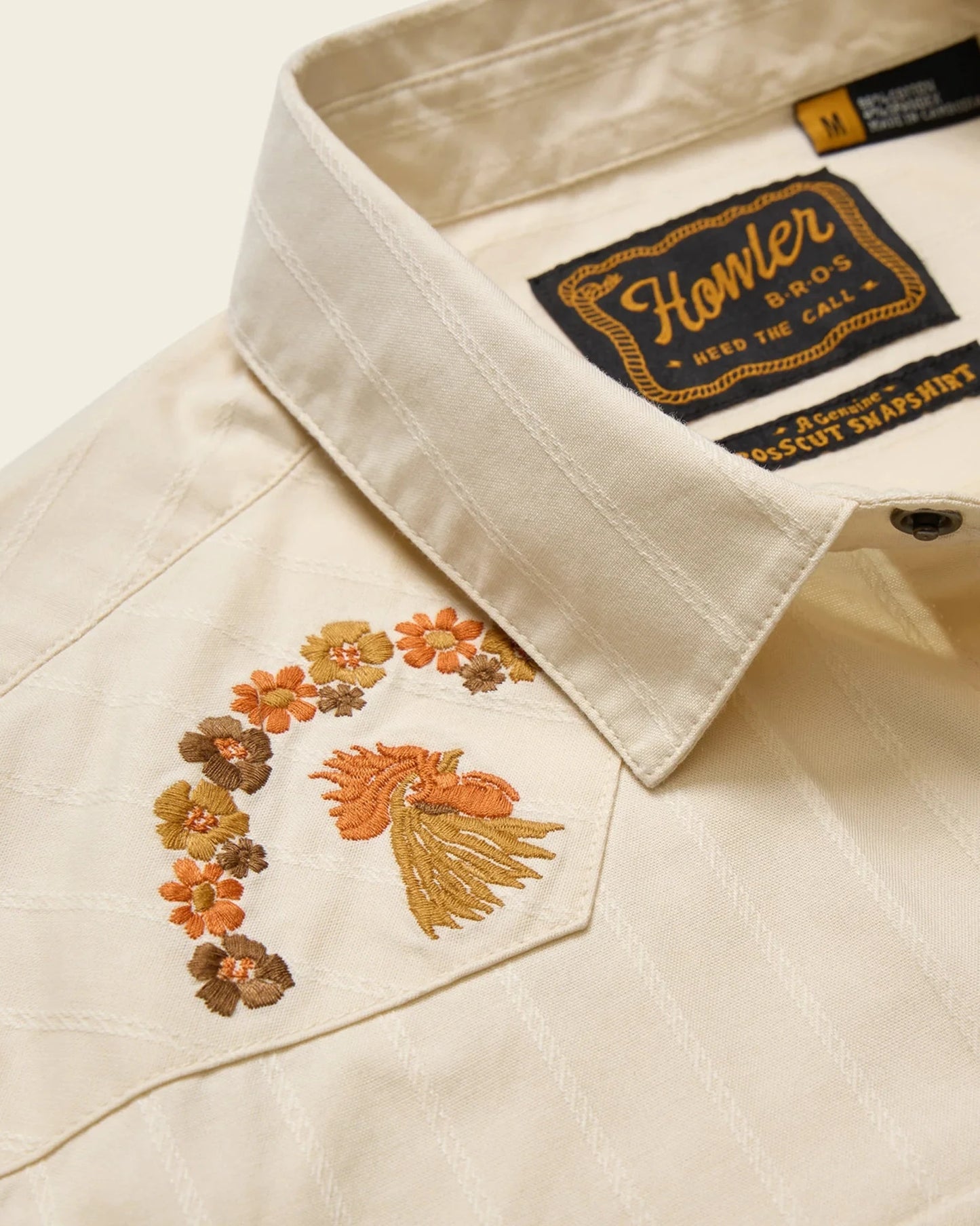 Close-up of a beige shirt with floral embroidery and 'Howler Bros' label.