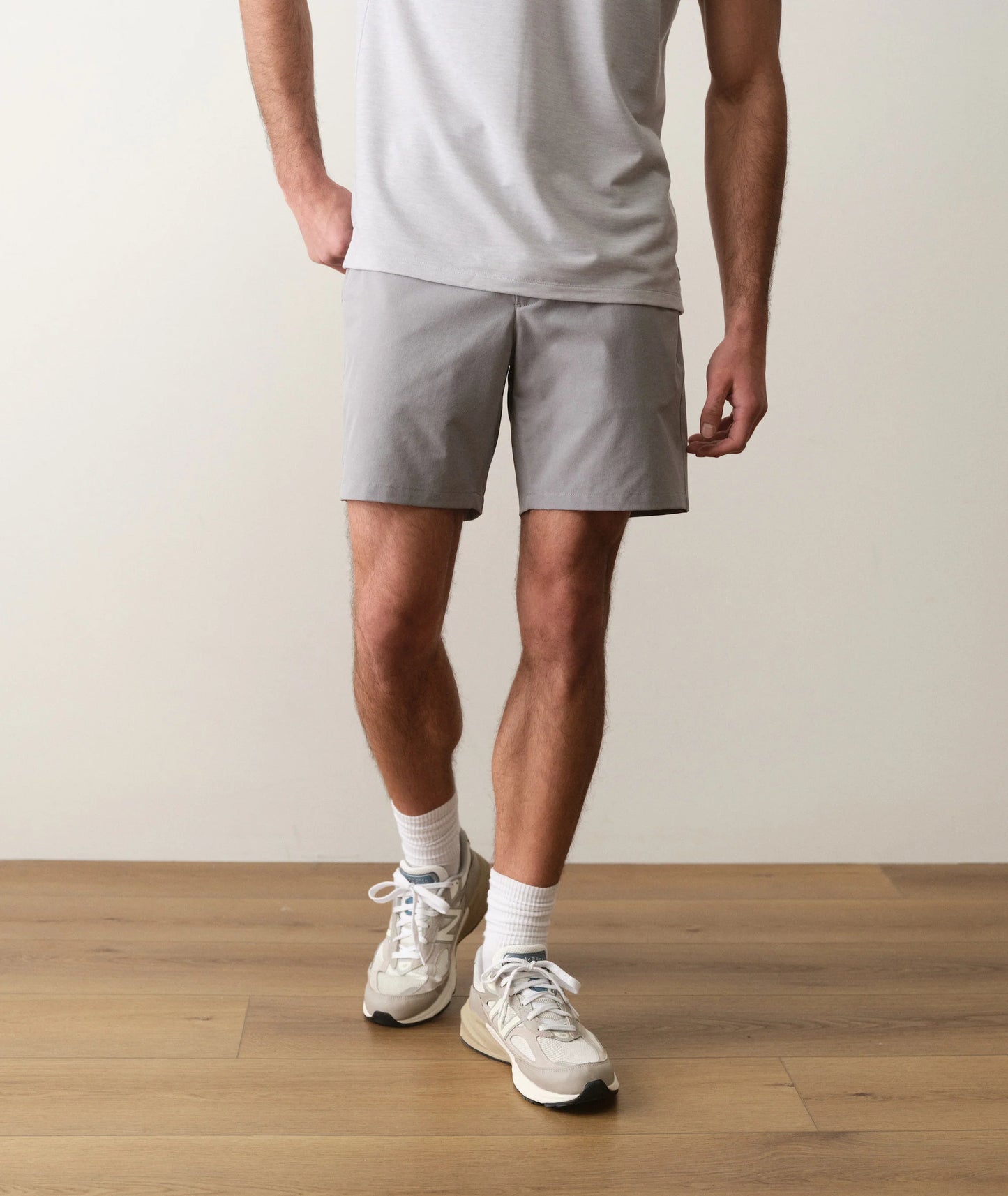 Person wearing gray shorts and white sneakers on a wooden floor with a neutral background