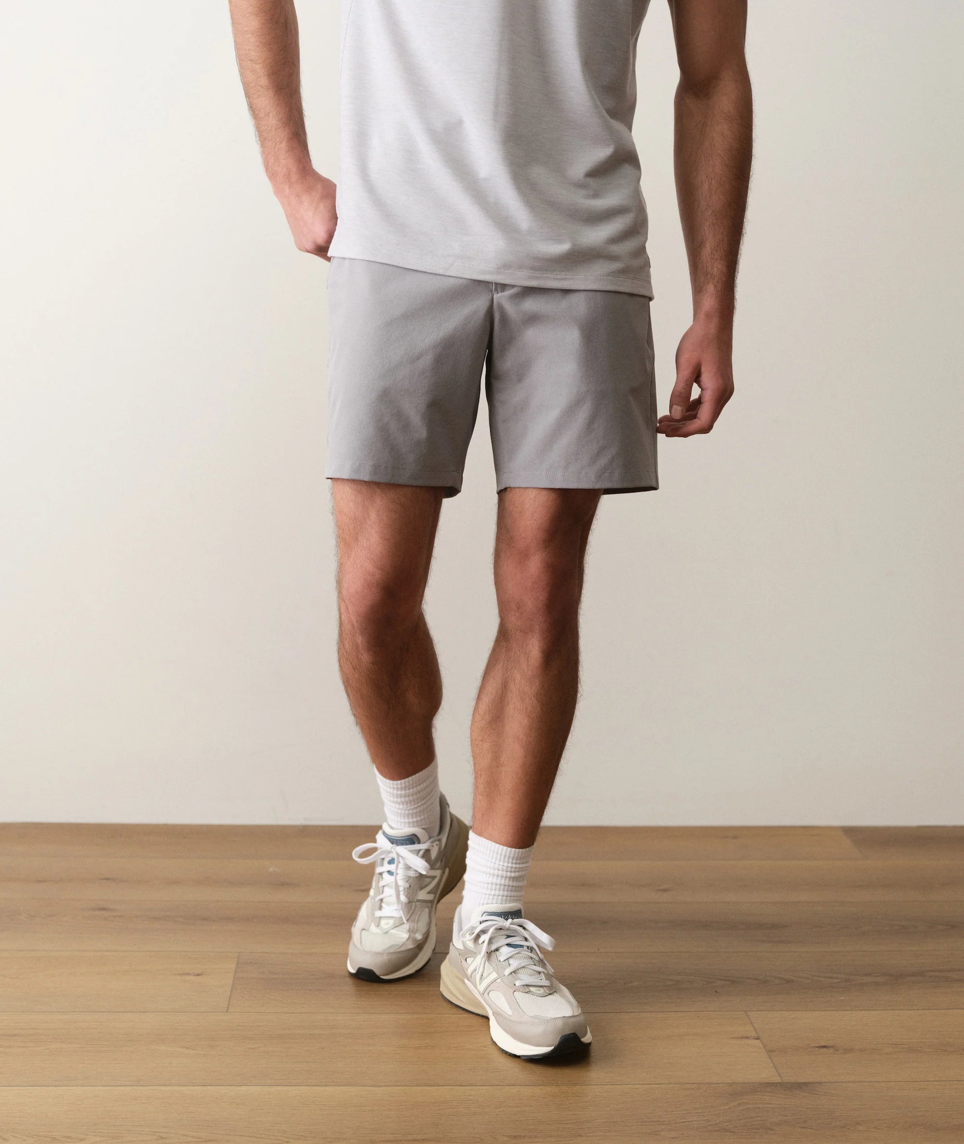 Person wearing gray shorts and white sneakers on a wooden floor with a neutral background