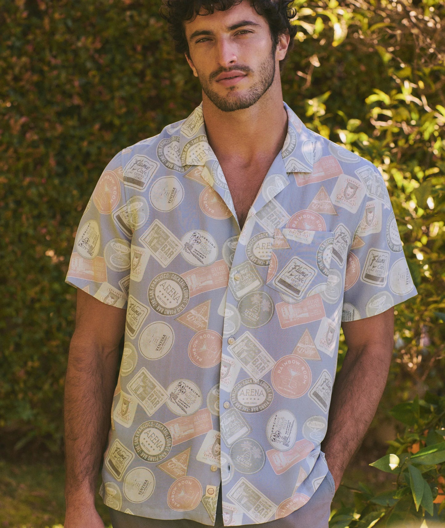 Man wearing a patterned shirt outdoors with greenery in the background