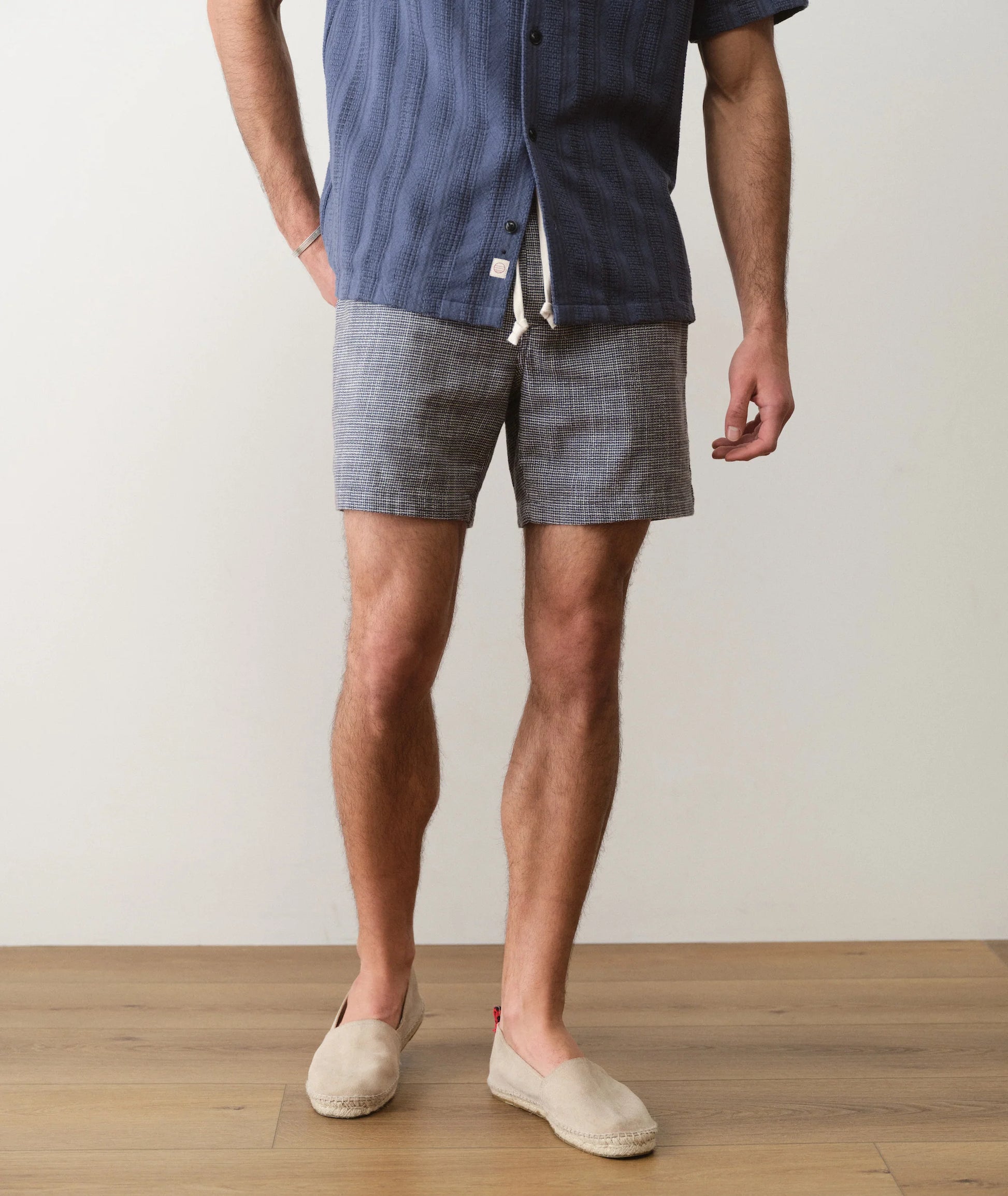 Person wearing a blue shirt and gray checkered shorts on a wooden floor.