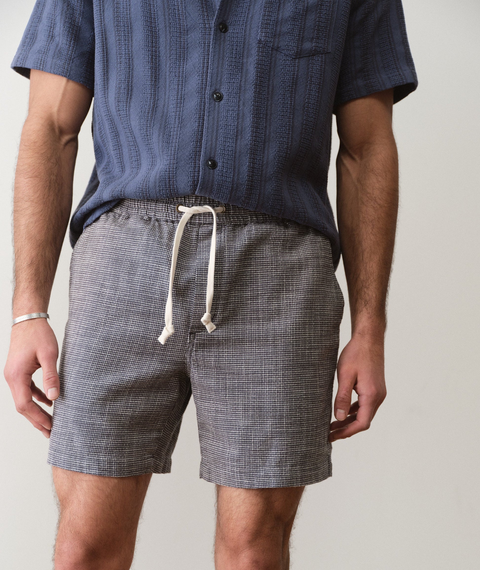 Person wearing a blue shirt and gray shorts with a white drawstring on a plain background