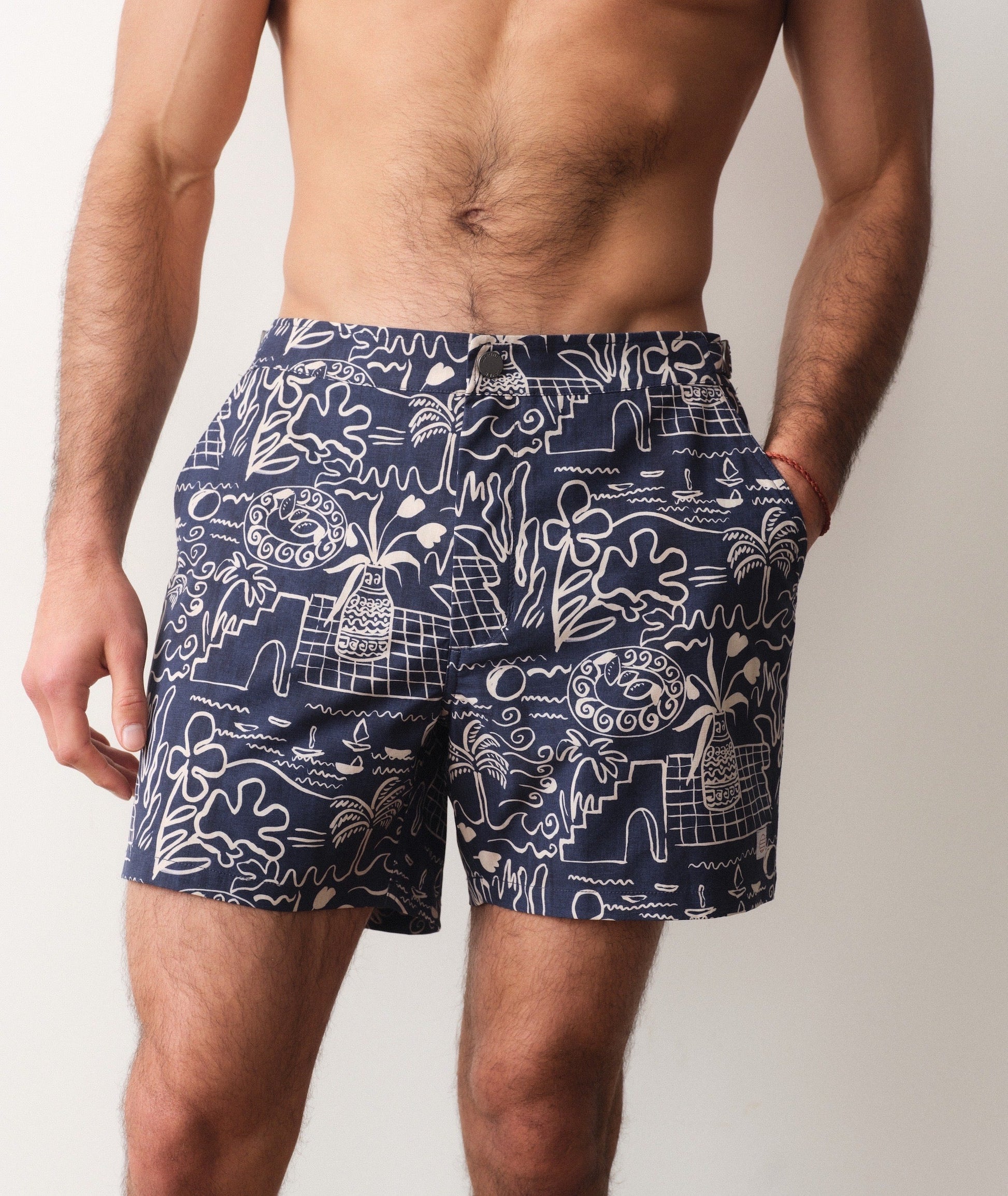 Navy blue swim shorts with white abstract pattern worn by a person on a plain background