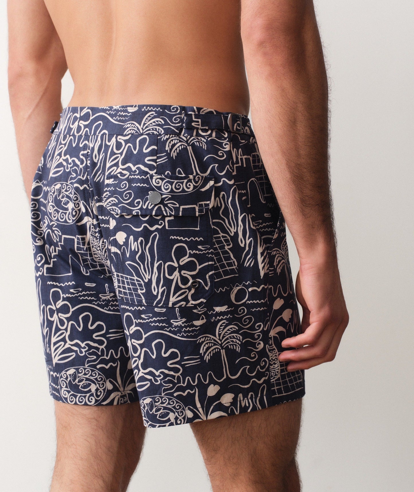 Person wearing navy blue swim shorts with white abstract patterns on a plain background