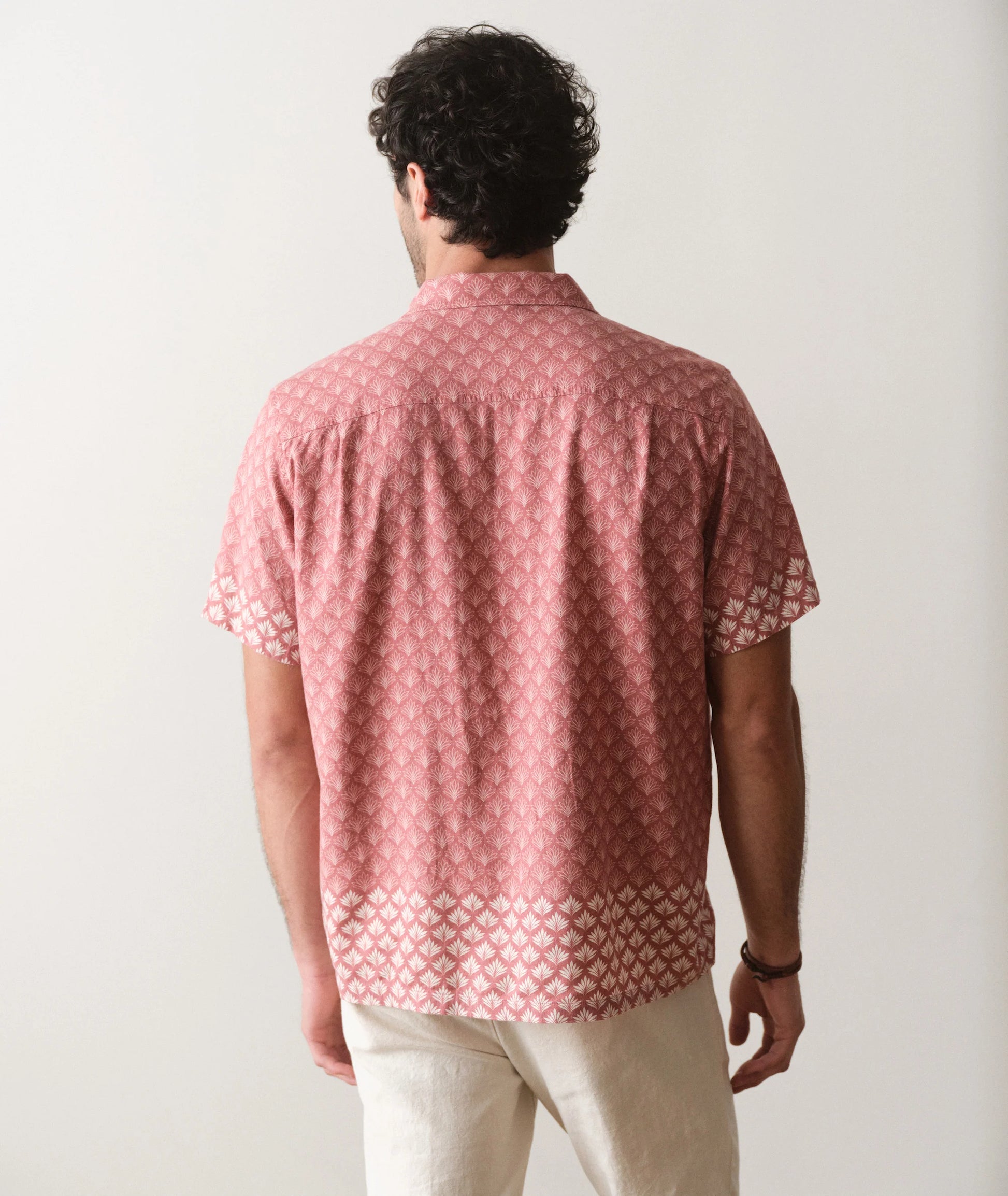 Man wearing a pink patterned shirt and beige pants against a white background