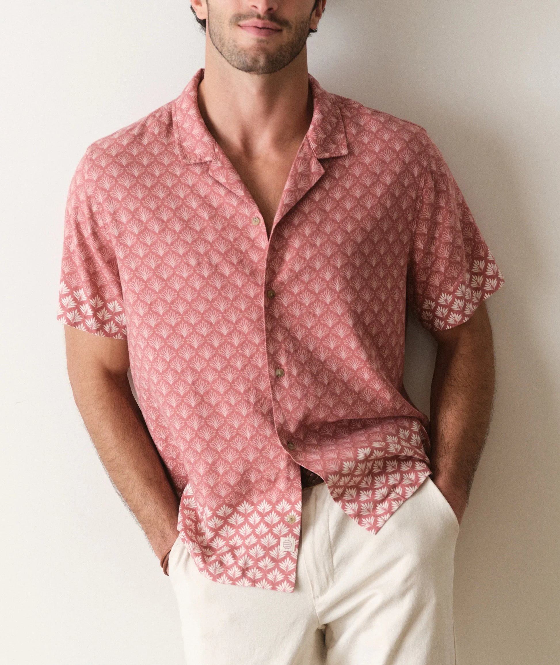 Man wearing a pink patterned shirt and white pants against a plain background