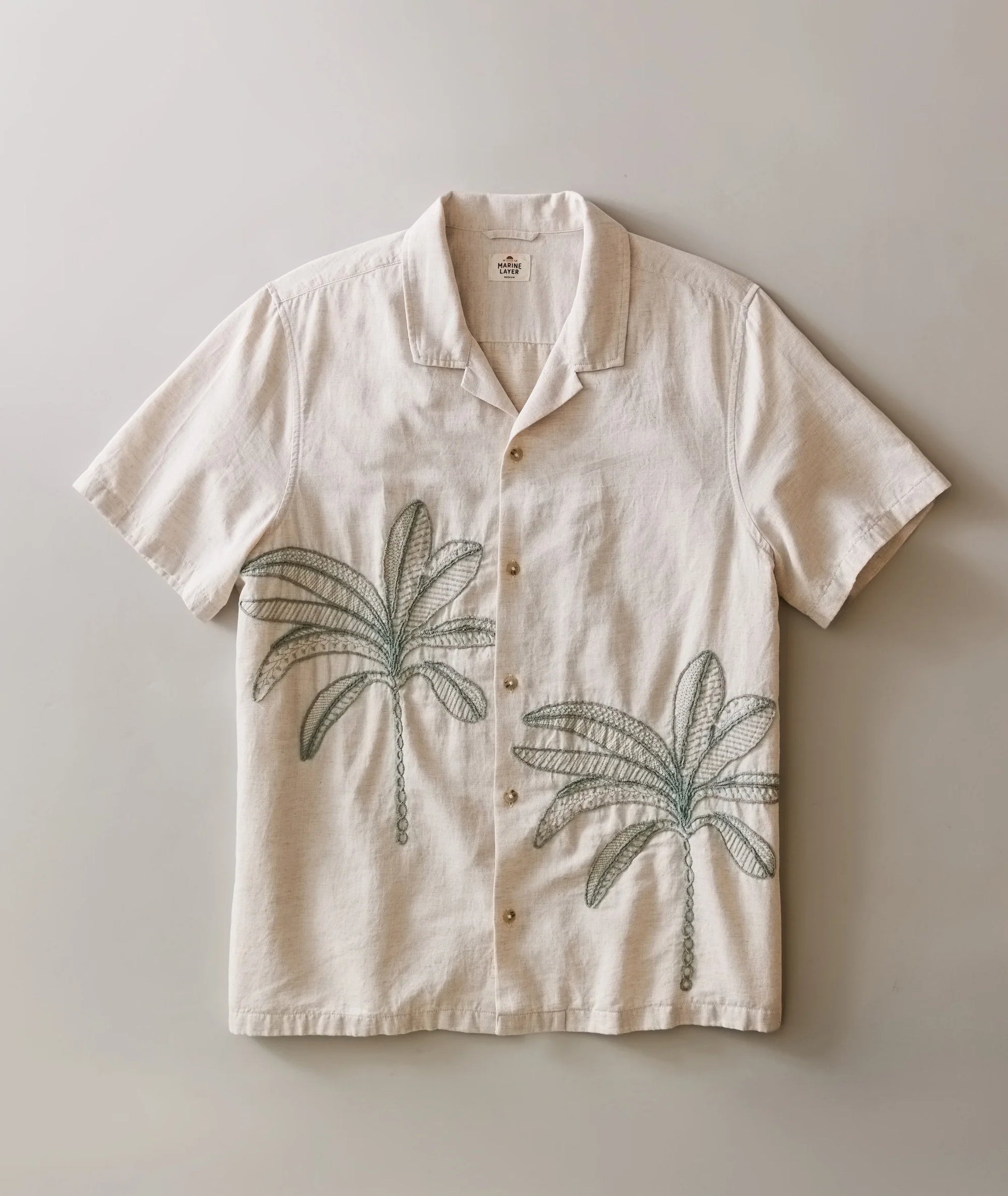 Beige shirt with palm tree designs on a plain background