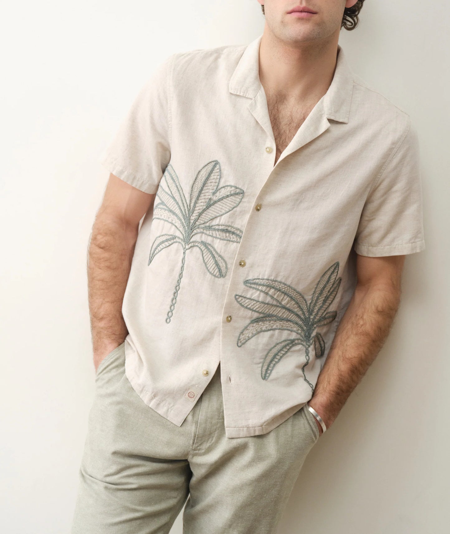 Man wearing a beige shirt with palm tree designs against a plain background