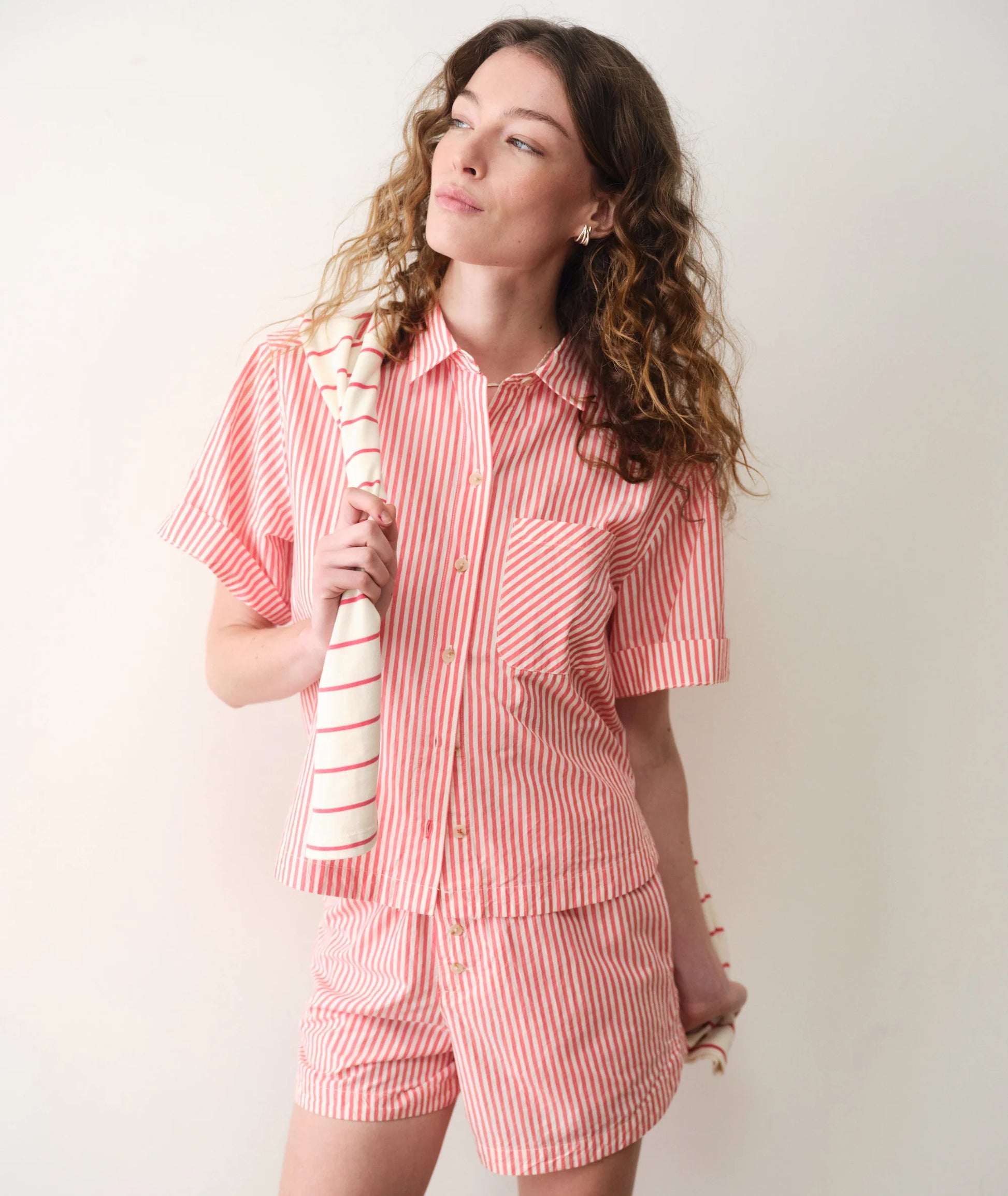 Woman wearing a red and white striped pajama set holding a striped towel.