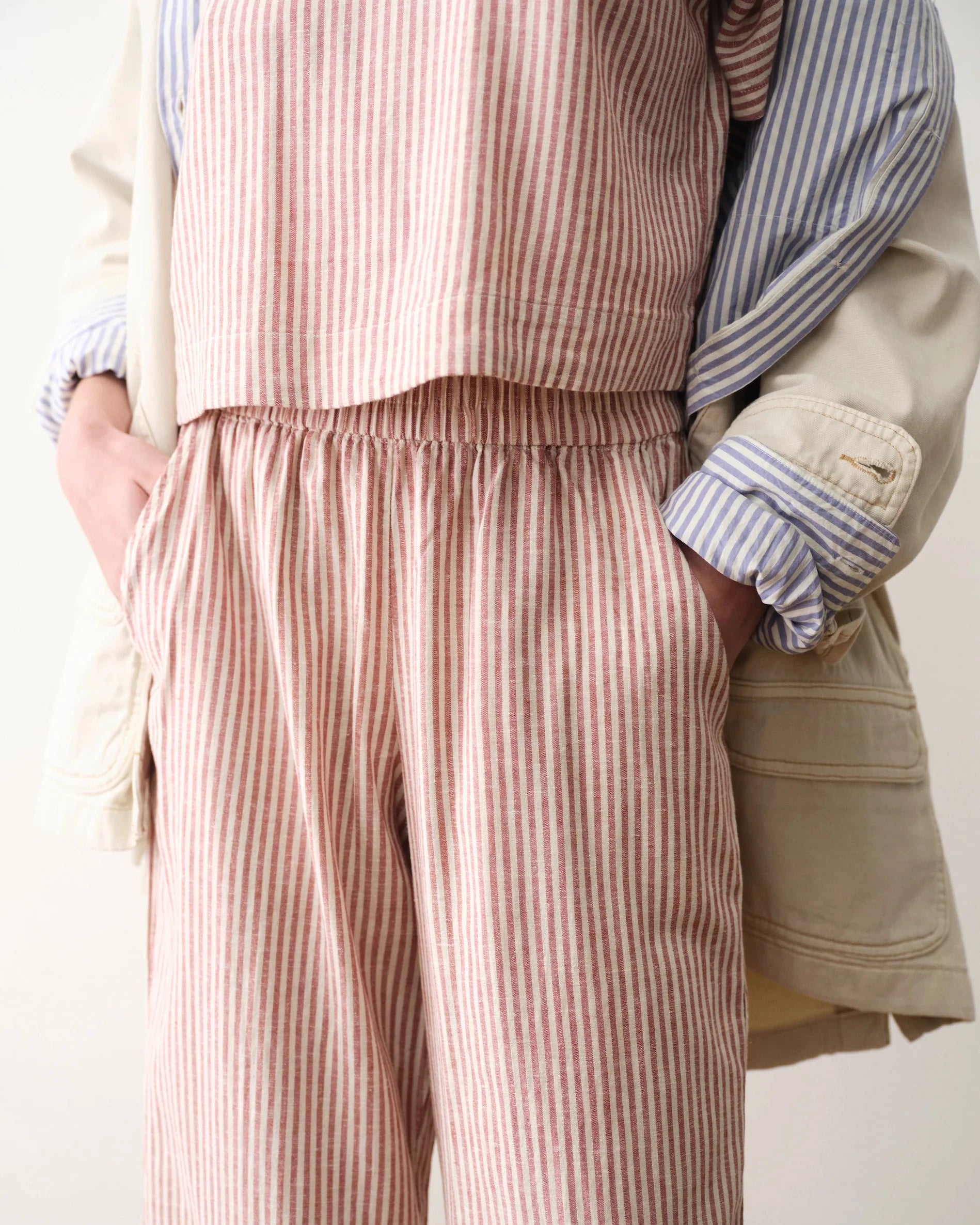 Person wearing a striped apron over a shirt with a beige jacket on a light background