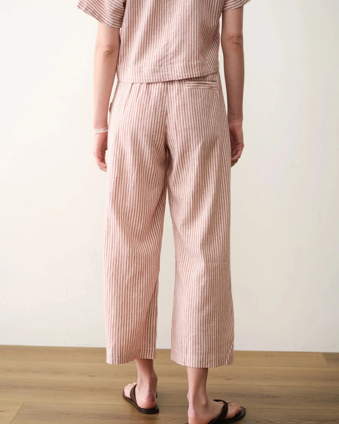 Person wearing a striped shirt and pants on a wooden floor with a white wall background