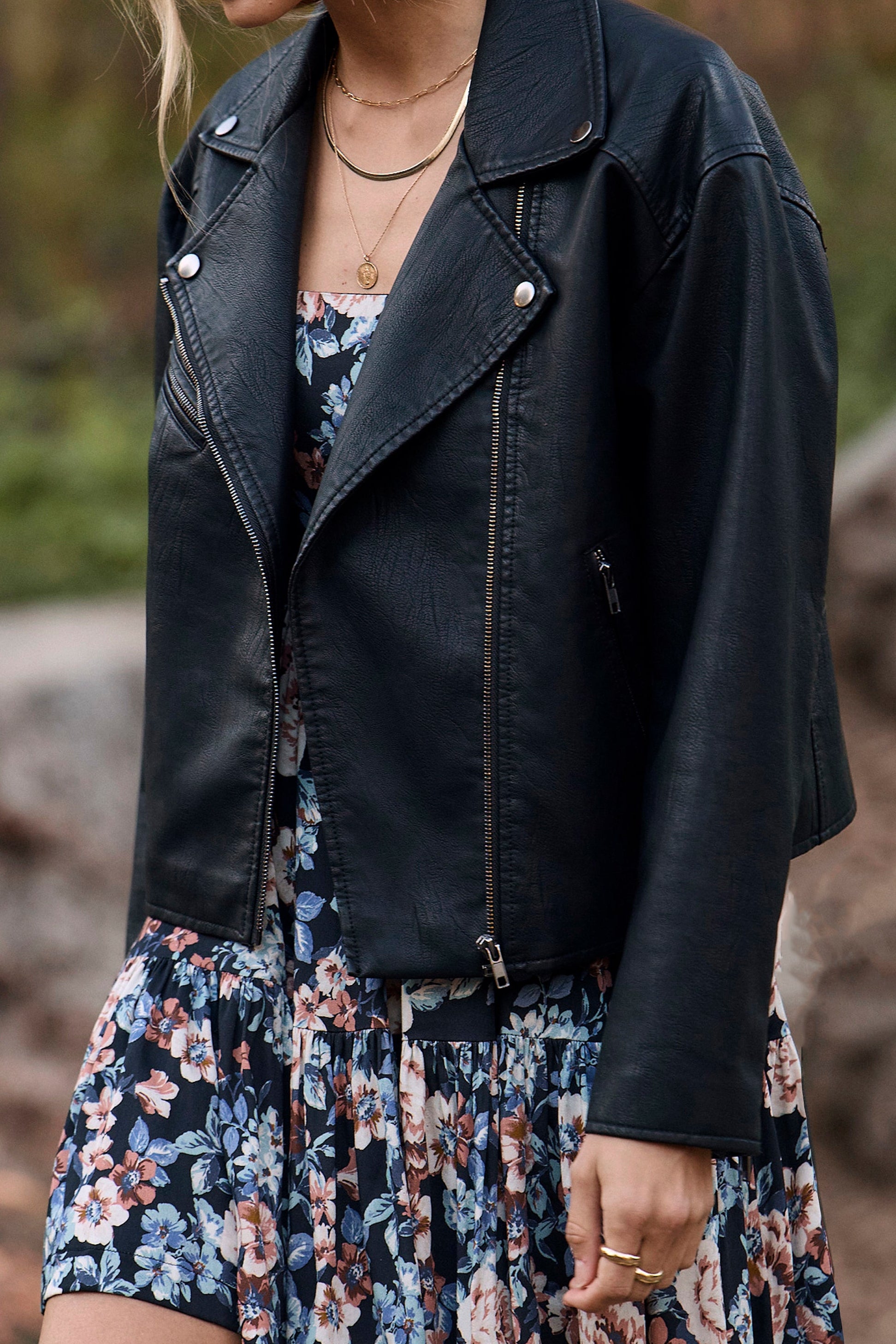 Woman wearing a black leather jacket over a floral dress in an outdoor setting