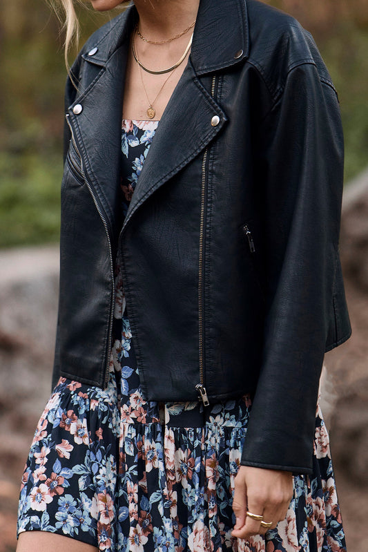 Woman wearing a black leather jacket over a floral dress in an outdoor setting
