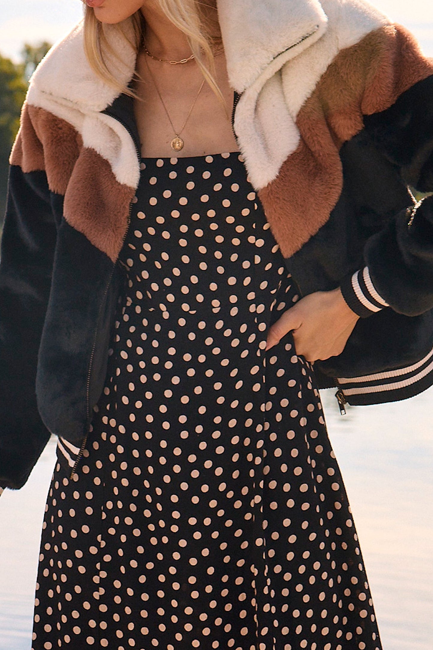 Woman wearing a stylish jacket with a fur-lined hood by a lake