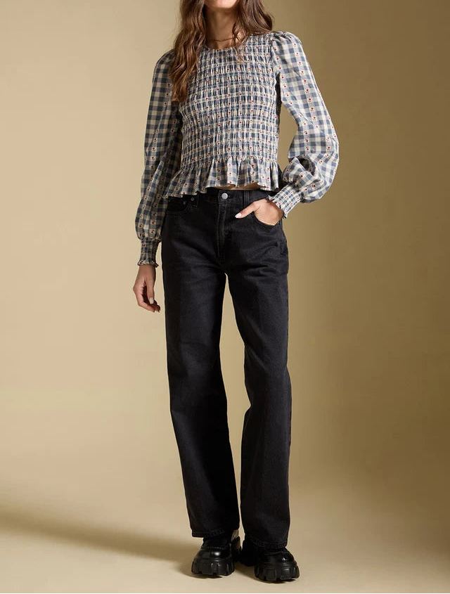 Woman wearing a plaid blouse and black pants against a beige background