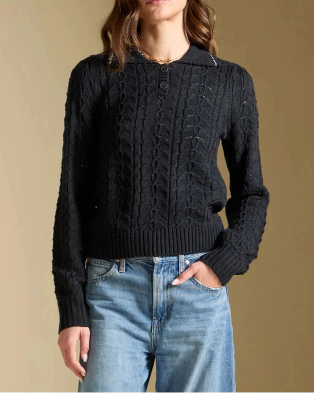 Woman wearing a black cable knit sweater and blue jeans against a beige background
