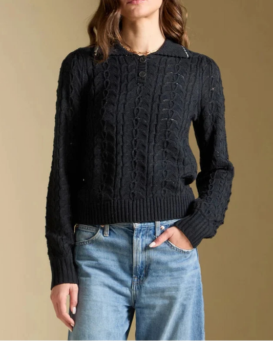 Woman wearing a black cable knit sweater and blue jeans against a beige background
