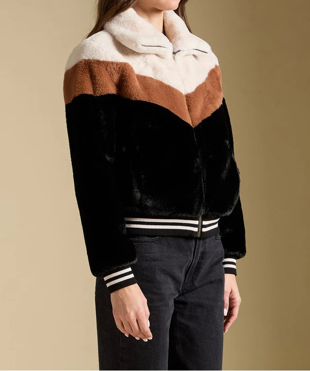 Woman wearing a black, brown, and white jacket against a beige background