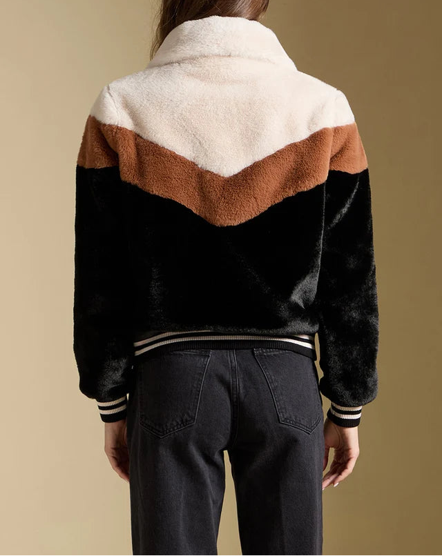 Person wearing a black, brown, and white jacket with a beige background