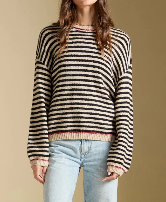 Woman wearing a black and beige striped sweater with light blue jeans on a beige background