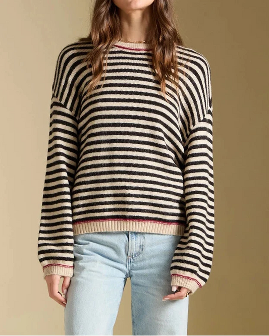Woman wearing a black and beige striped sweater with light blue jeans on a beige background