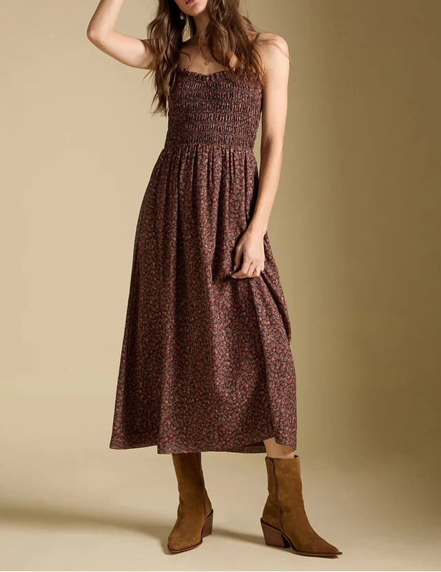Woman wearing a brown patterned dress and white hat against a beige background