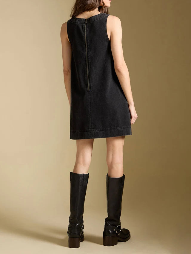Woman wearing a black sleeveless dress and black knee-high boots against a beige background