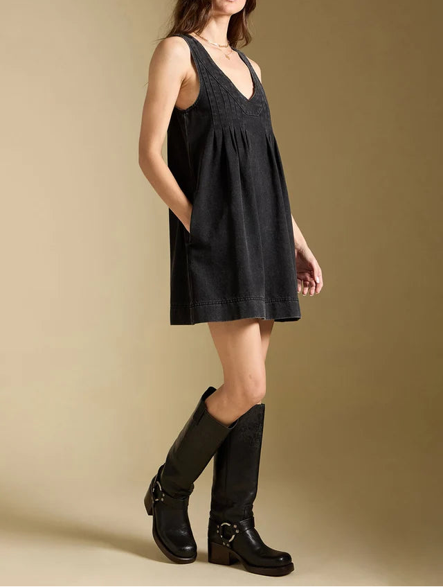 Woman wearing a black sleeveless dress and black knee-high boots against a beige background