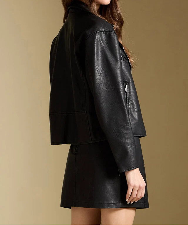Woman wearing a black leather jacket and skirt against a beige background