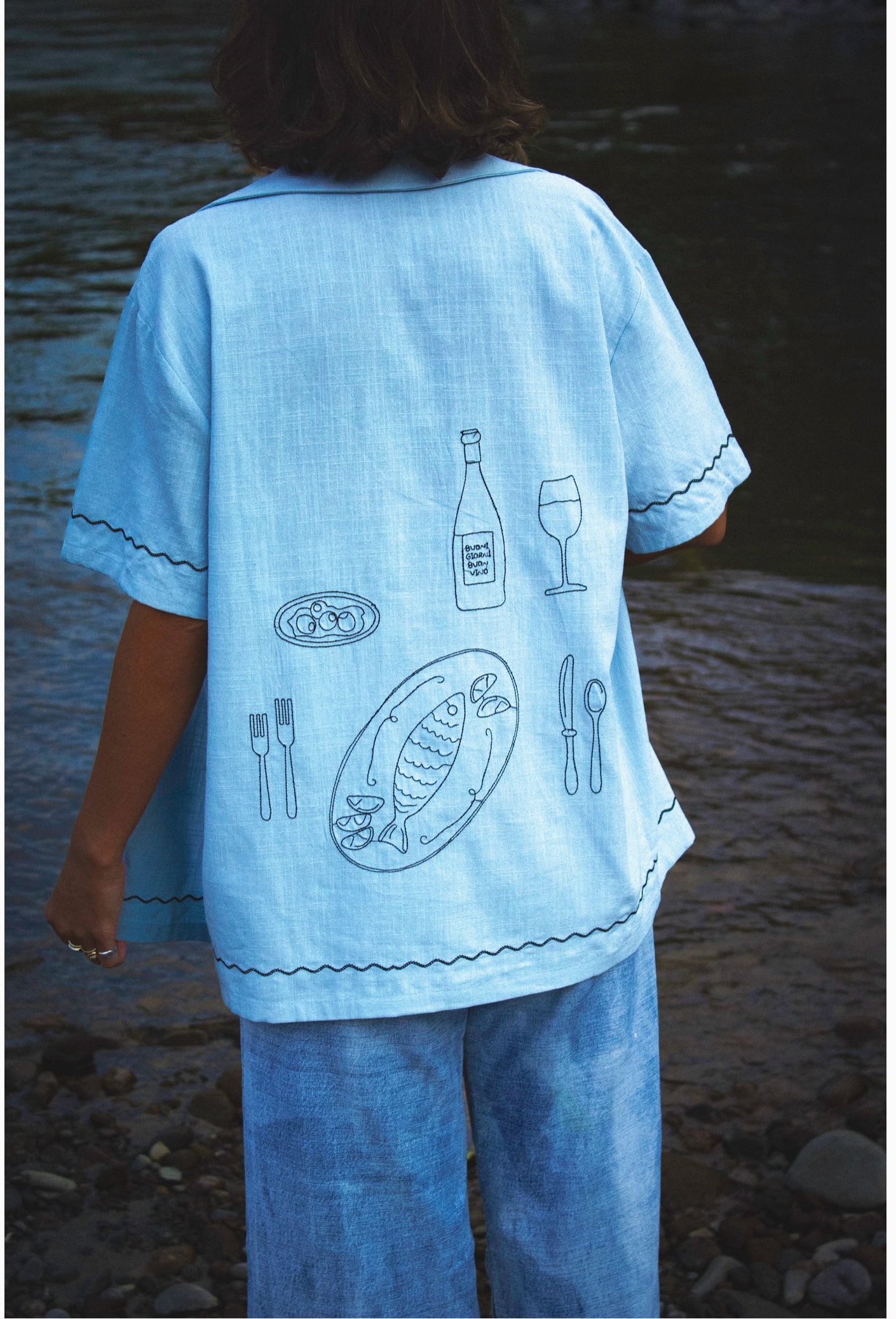 A person is turned around showcasing the embroidery on the back of this soft blue woven shirt