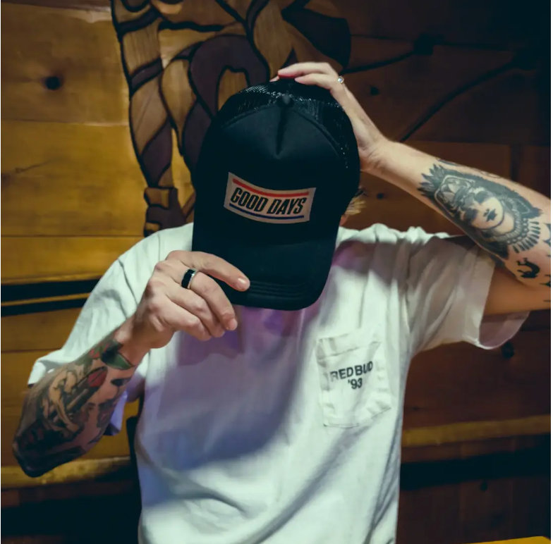 Man with tattoos covering face with black GOOD DAYS trucker cap.