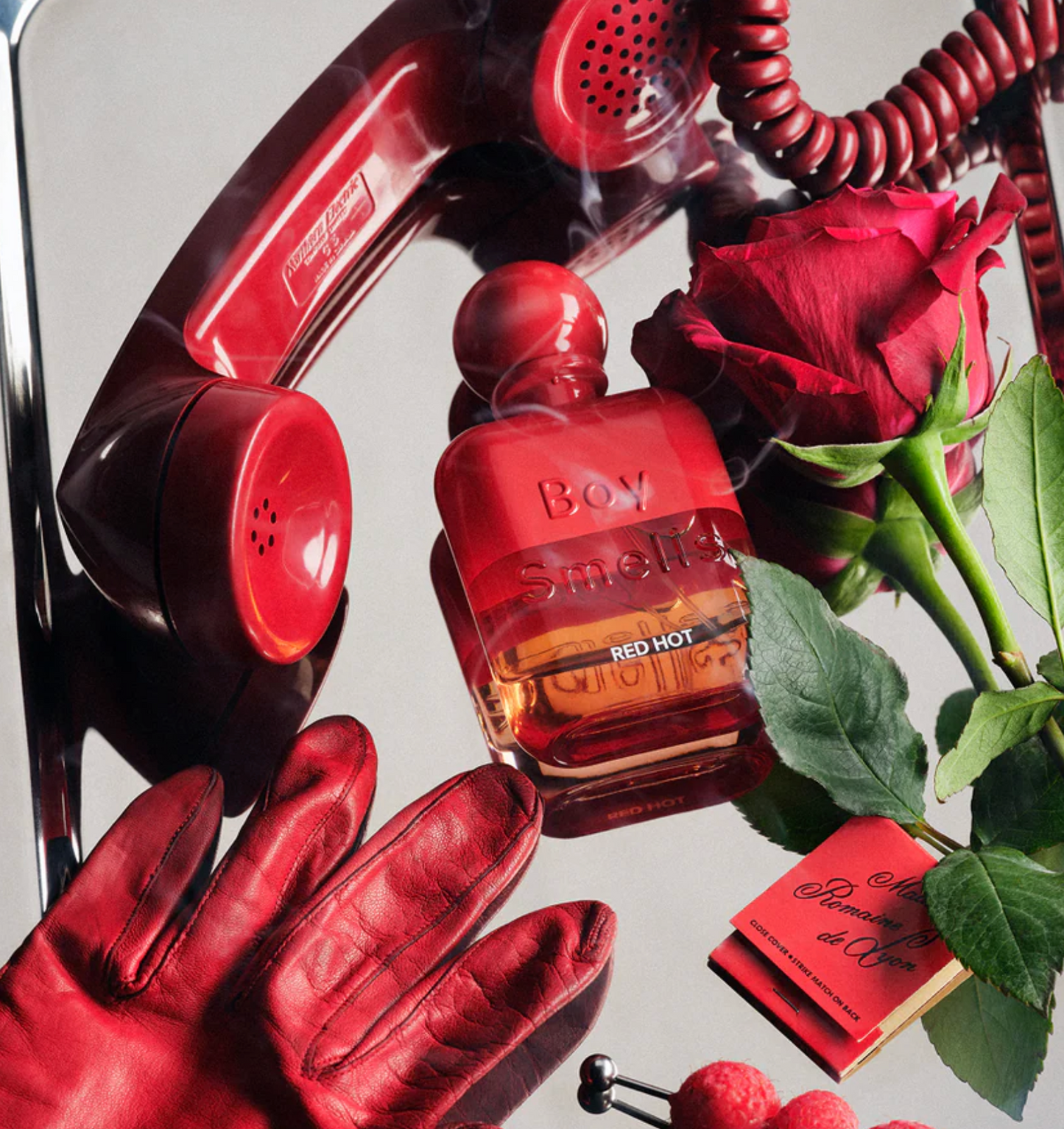 Red perfume bottle with roses, gloves, and a phone on a reflective surface