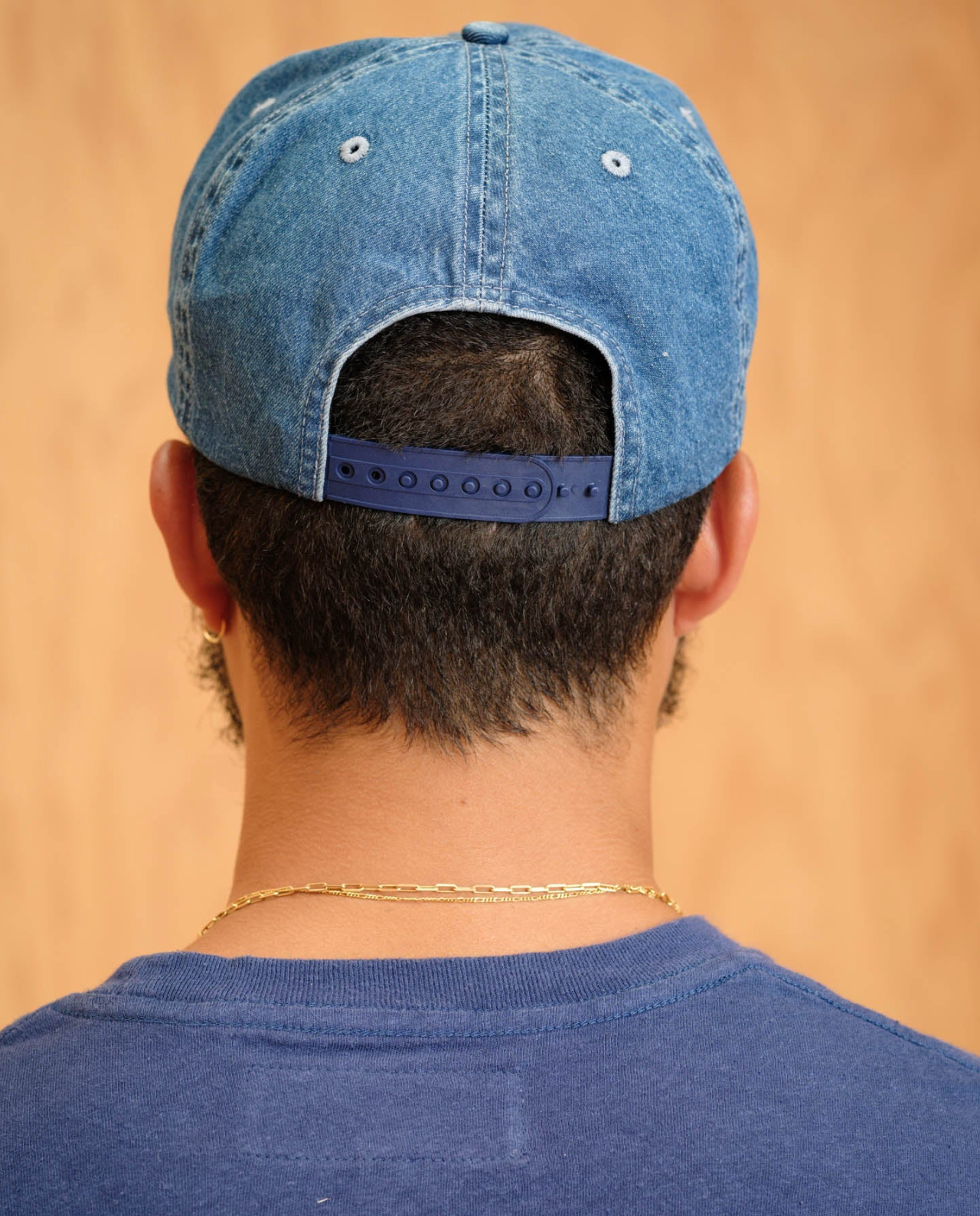 Person wearing a blue denim cap and shirt against a beige background