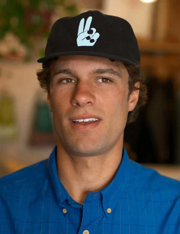 Man wearing a black cap with a white logo, smiling indoors.