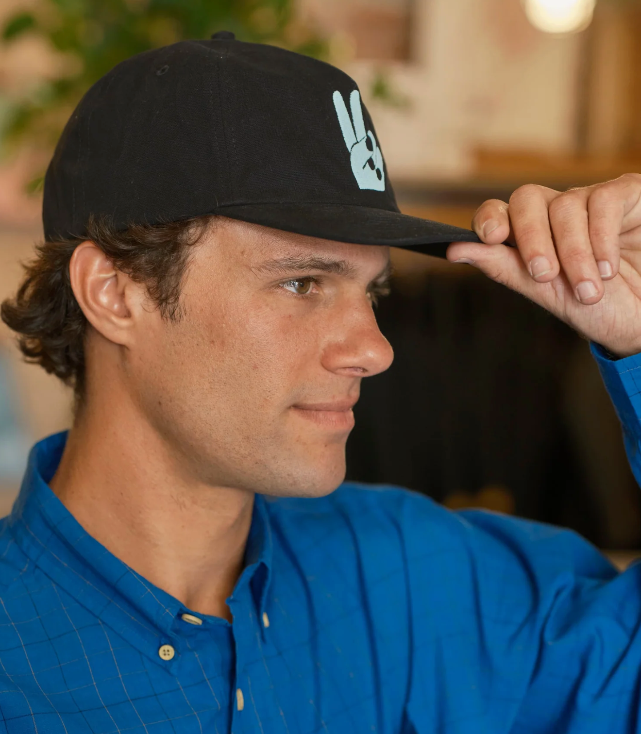 Man wearing a black cap with a logo, adjusting it with his hand.